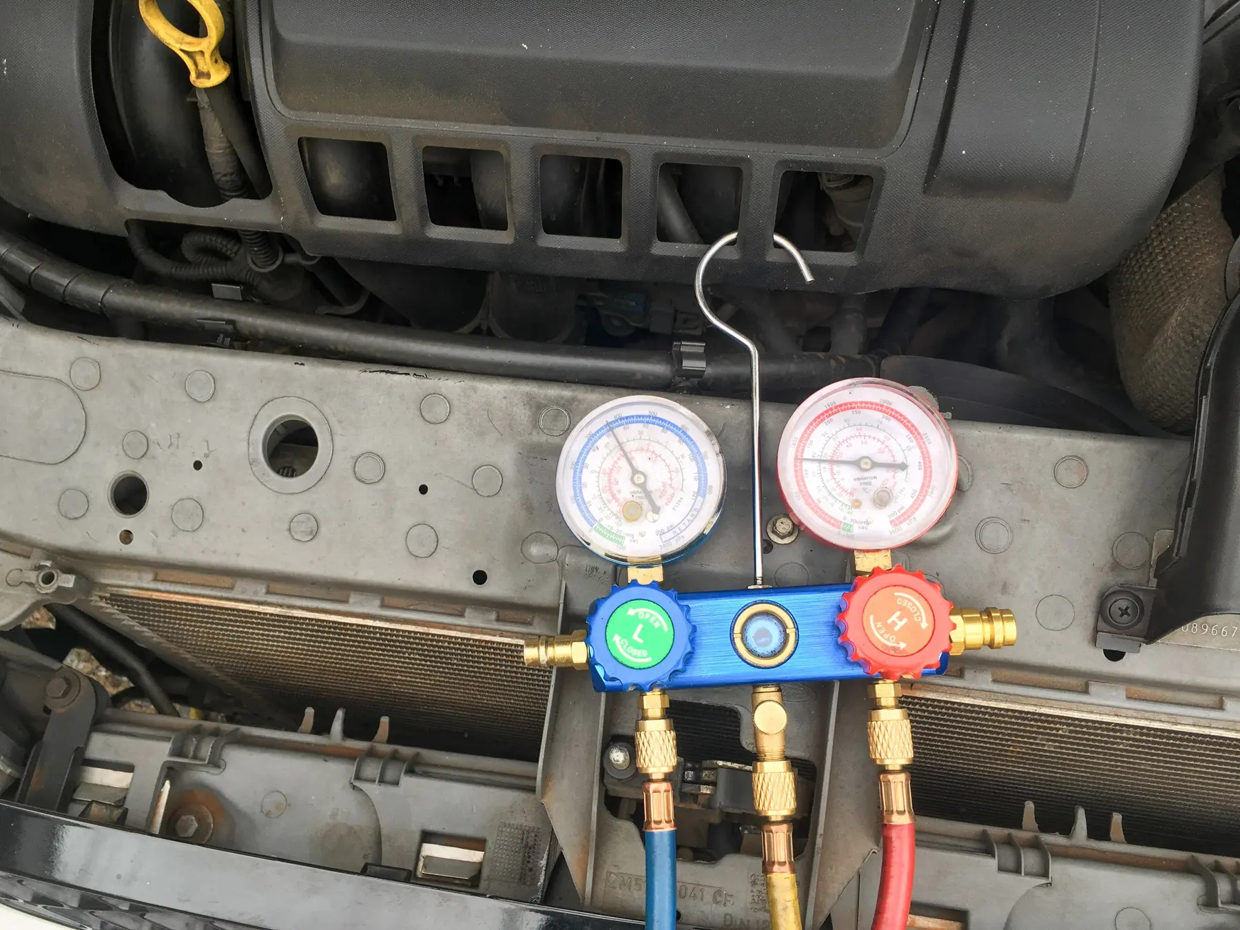 Set tolok manifold dengan dail biru dan merah digantung di bahagian hadapan kereta semasa mengisi semula gas penyaman udara