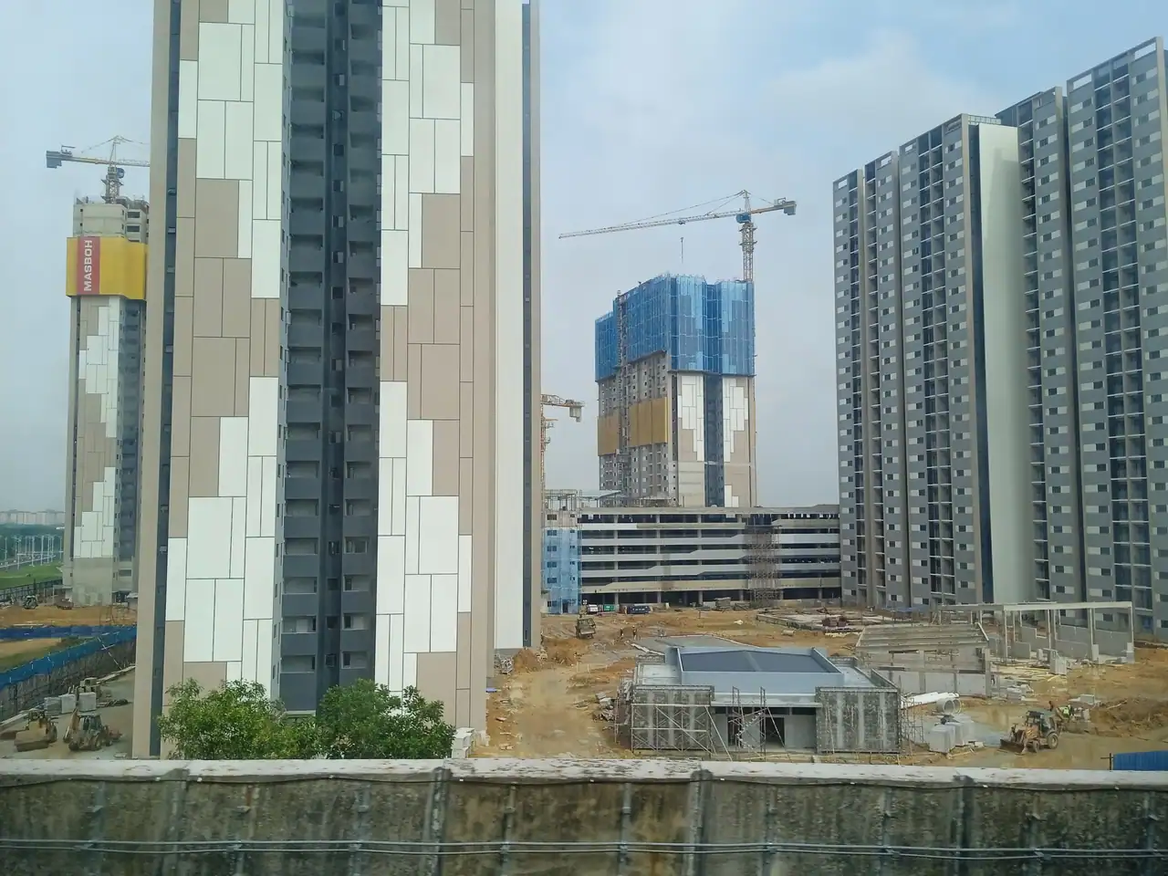 Idaman Kwasa Damansara towers with cream and grey cladding, a crane still on the last tower, April 2026