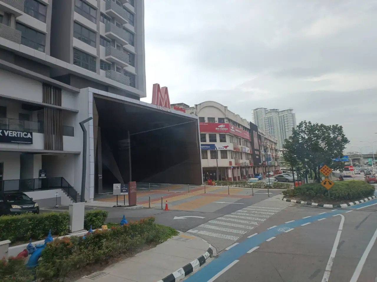 The dark canopy entrance to M Vertica with the red M sign above the shophouses