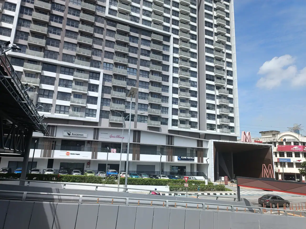 M Vertica tower and podium beside the road with cars parked below
