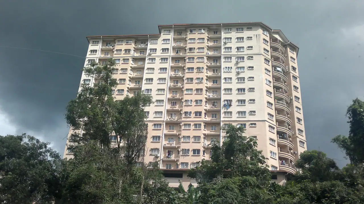 A tall pink and cream Oakleaf Park block seen through trees in Taman Bukit Jaya