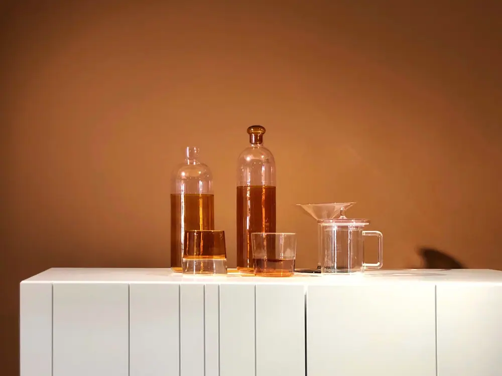 Amber glass bottles and a small glass funnel on a white counter against a warm brown wall