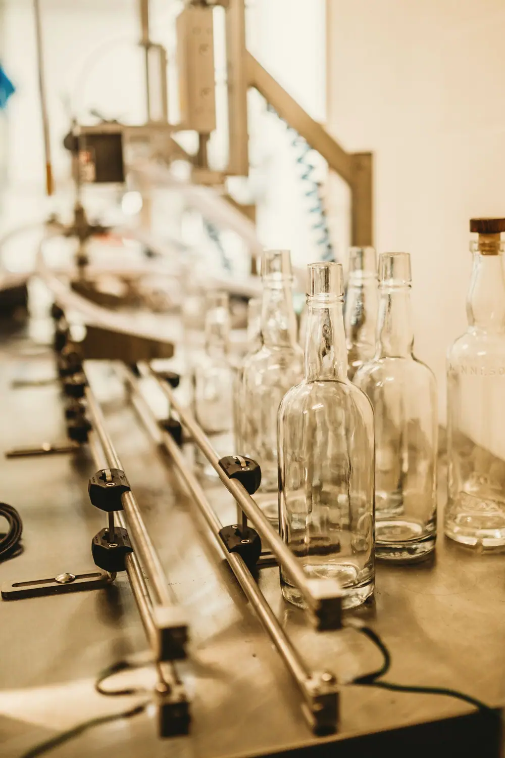 Rows of empty glass bottles moving along a filling line in warm light