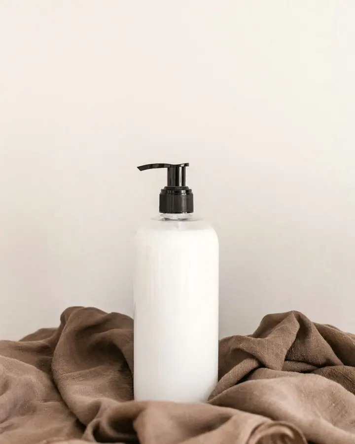 White pump bottle with a black pump on a warm beige surface, beside folded brown cloth