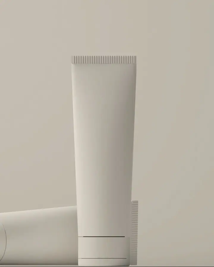 White matte cosmetic tube standing upright beside a second tube lying on a warm grey surface